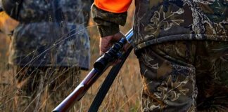 Hunter in camouflage holding a rifle in tall grass