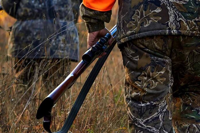 shutterstock_427671988 Hunter in camouflage holding a rifle in tall grass