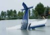A submerged airplane partially in a lake with trees in the background