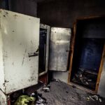 Abandoned room with open, rusted refrigerators and a dark doorway