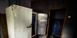 Abandoned room with open, rusted refrigerators and a dark doorway