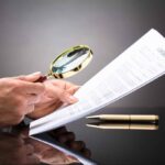 Historic Tradition Test Wrecks Knife Ban Hands holding magnifying glass over contract document
