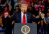Donald Trump speaking at a rally podium with arms raised