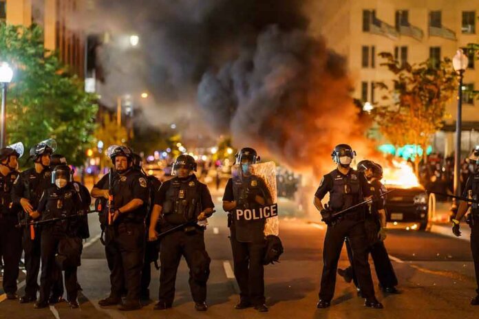 Christian Jones and Teddy Williams among police line at night protest with fire and smoke