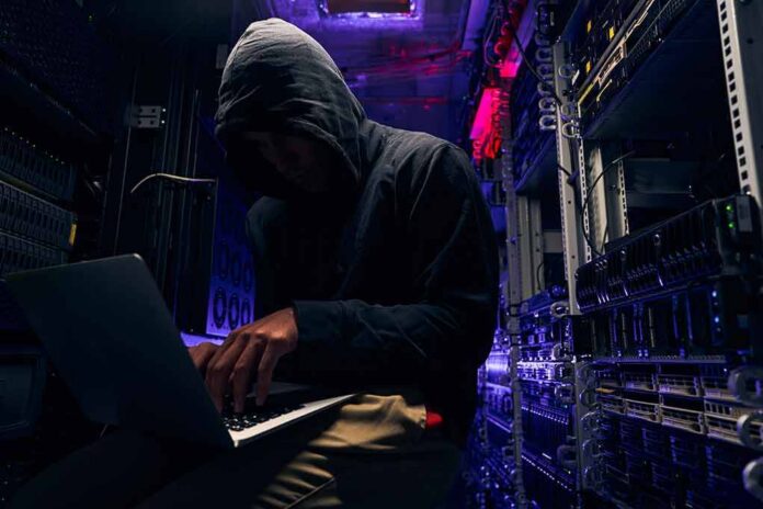 Hooded person using a laptop in a dark server room