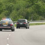 Police car with flashing lights following a minivan on a highway