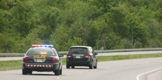 Police car with flashing lights following a minivan on a highway