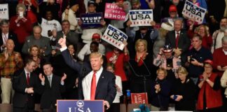 Donald Trump addresses a rally crowd at a podium, raising his fist
