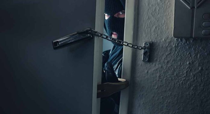 masked intruder peeking through chained door
